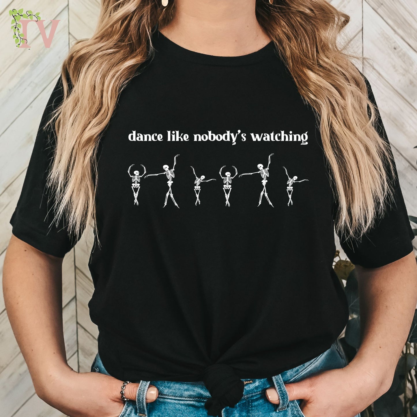 This is a white screen print transfer depicting 6 cute skeletons dancing; A fun quote to dance like nobody's watching is placed at the top of the design.